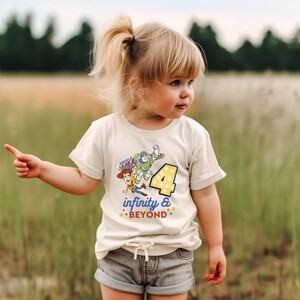 Puede incluir: Una camiseta blanca con un gr&aacute;fico de Woody y Buzz Lightyear de Toy Story. El gr&aacute;fico incluye el n&uacute;mero 4 y el texto "infinity & BEYOND". La camiseta la lleva puesta un ni&ntilde;o.
