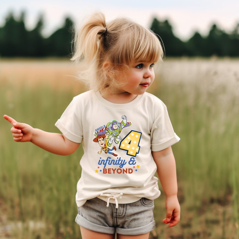 Puede incluir: Una camiseta blanca con un gr&aacute;fico de Woody y Buzz Lightyear de Toy Story. El gr&aacute;fico incluye el n&uacute;mero 4 y el texto "infinity & BEYOND". La camiseta la lleva puesta un ni&ntilde;o.