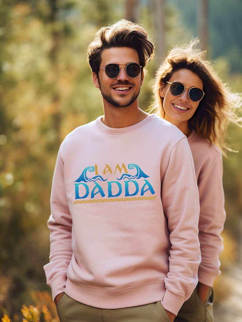 May include: A pink sweatshirt with a blue and yellow graphic that says "I AM DADDA" with waves and a gold border.