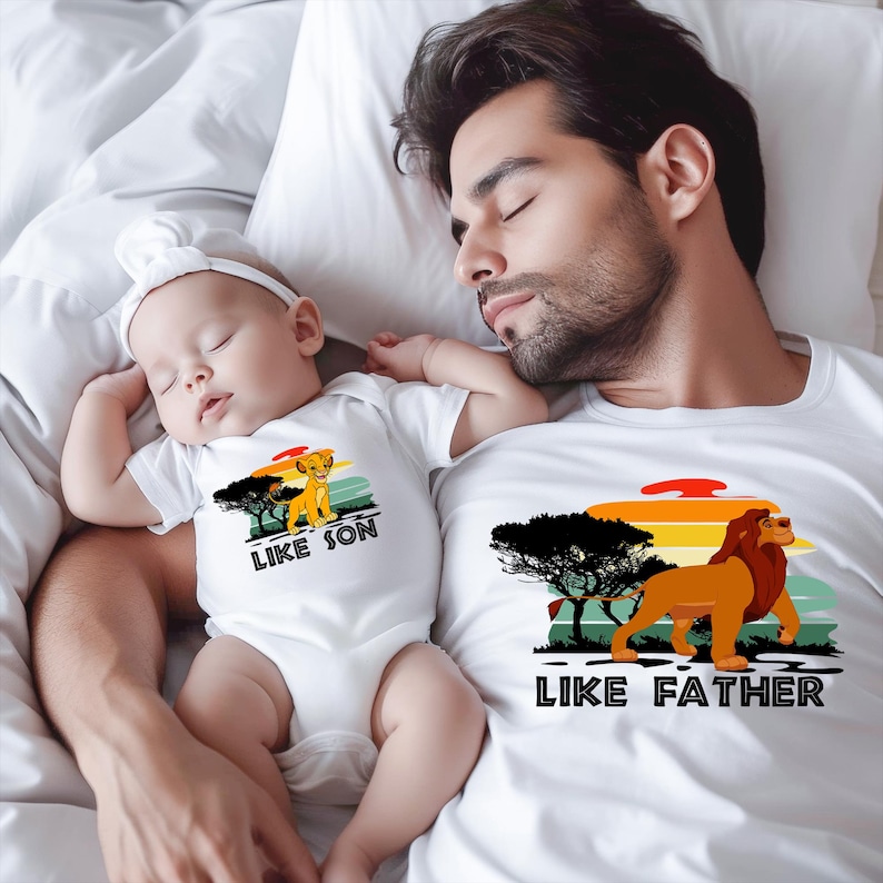May include: A white t-shirt with a lion graphic and the text "Like Father, Like Son". A baby wearing a white onesie with a lion graphic and the text "Like Son" is sleeping on the chest of a man wearing the t-shirt.