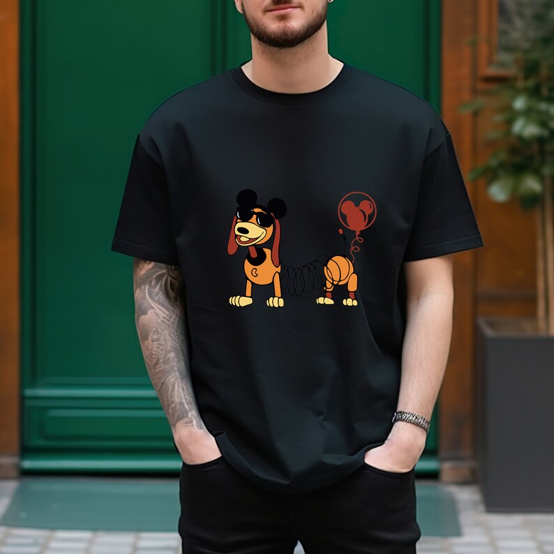 May include: A black t-shirt with a cartoon image of a brown and orange dog with a springy tail. The dog is wearing Mickey Mouse ears and a red balloon with Mickey Mouse ears is attached to its tail.