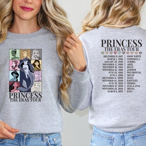 Puede incluir: Una sudadera gris con un estampado gr&aacute;fico de princesas Disney y el texto "Princess The Eras Tour". La parte posterior de la sudadera tiene una lista de princesas y sus fechas de lanzamiento.