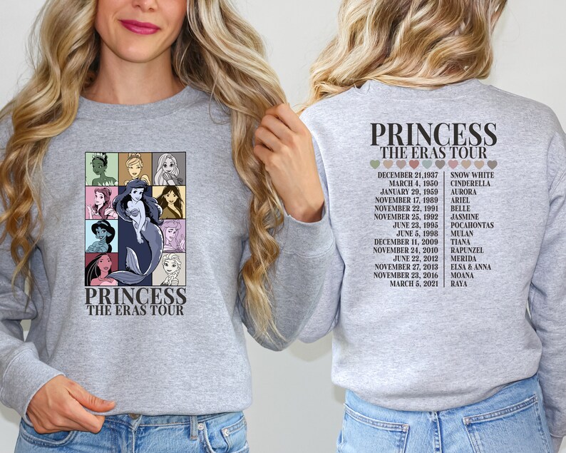 Puede incluir: Una sudadera gris con un estampado gr&aacute;fico de princesas Disney y el texto "Princess The Eras Tour". La parte posterior de la sudadera tiene una lista de princesas y sus fechas de lanzamiento.