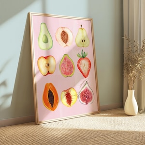 May include: A framed watercolor print featuring nine different sliced fruits on a pink background. The fruits include an avocado, peach, pear, apple, guava, strawberry, papaya, peach, and fig. The frame is a light wood color.
