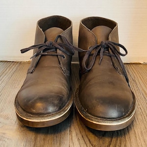 May include: A pair of brown leather ankle boots with laces. The boots have a worn look and are tied with brown laces.