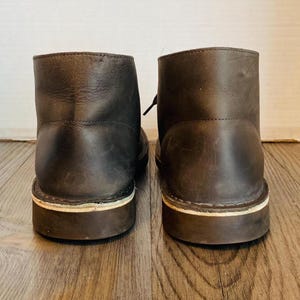 May include: A pair of brown leather ankle boots with white stitching around the soles.