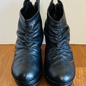 May include: A pair of black leather ankle boots with a zipper on the back. The boots have a platform sole and a slightly wrinkled look.