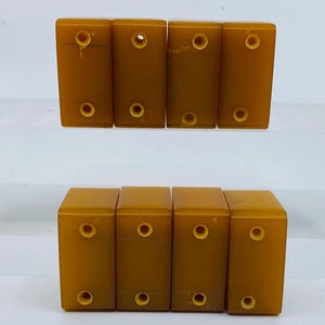 Op de afbeelding: Acht rechthoekige, amberkleurige dominostenen zijn in twee rijen gerangschikt. Elke domino heeft twee cirkelvormige gaten. De dominostenen hebben een gladde, glanzende afwerking en zijn gelijkmatig verdeeld.