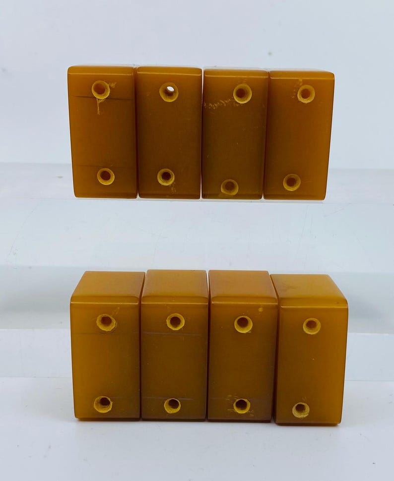 Op de afbeelding: Acht rechthoekige, amberkleurige dominostenen zijn in twee rijen gerangschikt. Elke domino heeft twee cirkelvormige gaten. De dominostenen hebben een gladde, glanzende afwerking en zijn gelijkmatig verdeeld.
