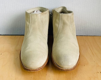 May include: A pair of light beige suede ankle boots with zipper closures on the sides. The boots have a brown leather sole and a rounded toe.