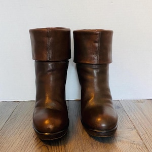 May include: A pair of brown leather boots with a folded-over cuff. The boots have a rounded toe and a platform sole. The leather has a glossy finish and a rich, dark brown color.