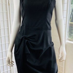 May include: A black sleeveless dress with a gathered skirt. The dress is fitted through the bodice and has a simple, rounded neckline.