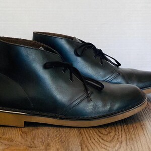 May include: A white ceramic mug with a black handle and the text "But First, Coffee" in a bold, black font. The mug is filled with a dark liquid, likely coffee, and sits on a light-colored surface.