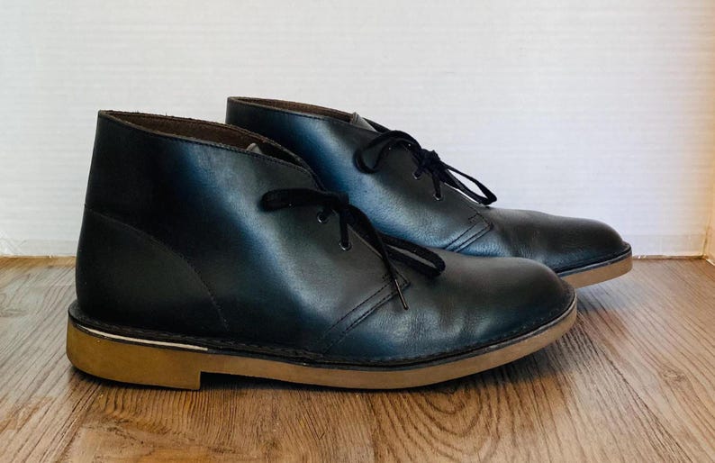 May include: A white ceramic mug with a black handle and the text "But First, Coffee" in a bold, black font. The mug is filled with a dark liquid, likely coffee, and sits on a light-colored surface.