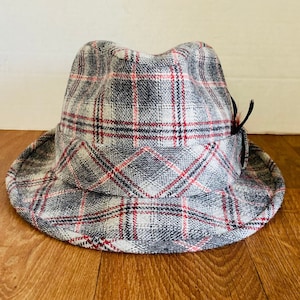 May include: A gray and red plaid fedora hat with a small black feather accent.