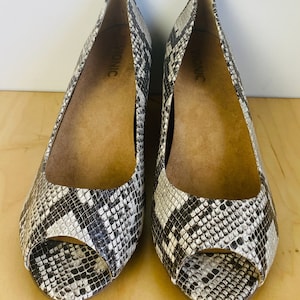 May include: A pair of black and white snakeskin peep-toe wedges with the brand name "Vionic" printed on the inside of each shoe.
