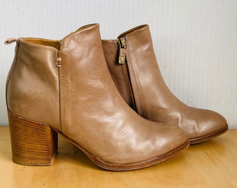 May include: A pair of brown leather ankle boots with a block heel. The boots have a zipper on the inside of each boot and a seam detail on the back of the boot.