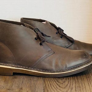 May include: A pair of brown leather ankle boots with laces. The boots have a cream-colored sole.