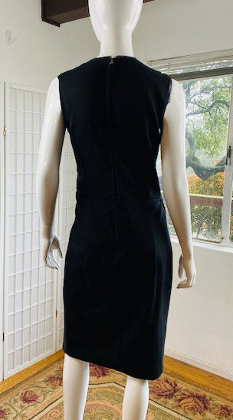 May include: A sleeveless black dress with a simple, fitted silhouette. The dress has a round neckline and a zipper closure in the back.
