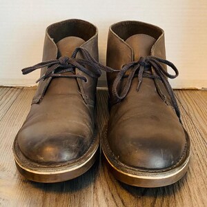 May include: A pair of brown leather ankle boots with laces. The boots have a worn look and are tied with dark brown laces.