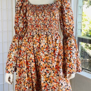 May include: A short-sleeved, orange, white, and black floral print dress with a smocked bodice and a square neckline. The dress has a loose fit and a flowy skirt.