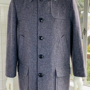 May include: A long-sleeved, gray wool coat with a button-up front and two large pockets. The coat has a unique design with a yoke and a flap on the back.