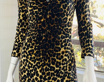 May include: A long-sleeved dress with a V-neckline and a leopard print pattern. The dress is displayed on a mannequin. The dress is a combination of black, brown, and tan colors.