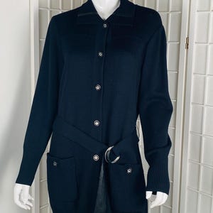 May include: A navy blue long-sleeved cardigan with a button-up front and a black leather belt. The cardigan has two pockets on the front and a ribbed texture.