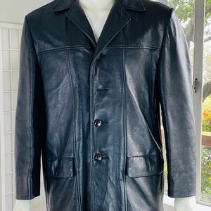 May include: A black leather jacket with a button-up front and two flap pockets. The jacket has a collar and long sleeves.