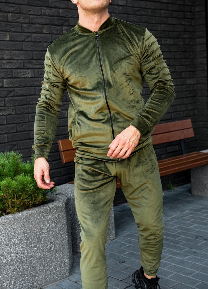 May include: A green velvet tracksuit with a zippered jacket and matching pants. The jacket has a stand-up collar and the pants have a drawstring waist.