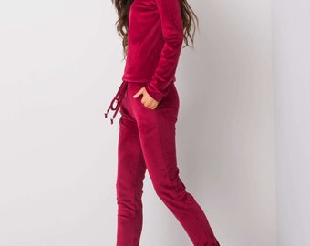 Könnte beinhalten: Ein roter Samt-Trainingsanzug mit einem Langarm-Oberteil und einer passenden Hose. Die Hose hat einen Kordelzugbund und das Model trägt weiße Turnschuhe.