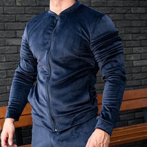 Op de afbeelding: Een donkerblauw velours trainingsjack met een ritssluiting. Het jack heeft een opstaande kraag en lange mouwen.