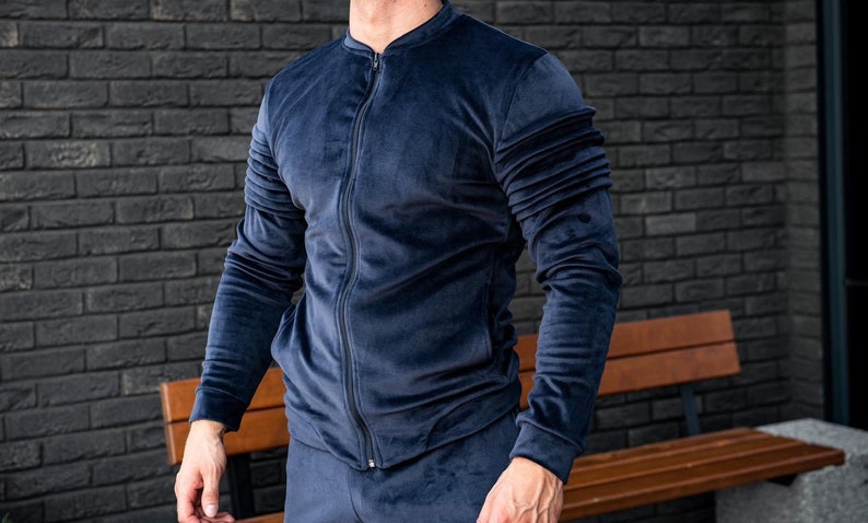 Op de afbeelding: Een donkerblauw velours trainingsjack met een ritssluiting. Het jack heeft een opstaande kraag en lange mouwen.