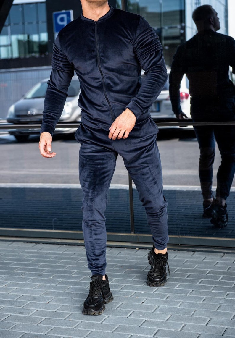 Op de afbeelding: Een donkerblauw velours trainingspak met een ritsjack en bijpassende broek. De persoon draagt zwarte sneakers.