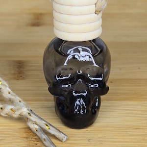 May include: A black skull-shaped car air freshener with a wooden lid and a beige and gold cord.