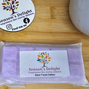May include: A purple wax melt bar in a clear plastic bag with a white label that reads "Season's Delight Fragrance for every season. Black Forest Gateau."