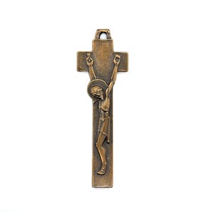 May include: Bronze-colored crucifix pendant featuring a detailed depiction of Jesus Christ on the cross. The figure is rendered with intricate details, including a halo and draped loincloth. The cross has a loop at the top for hanging.