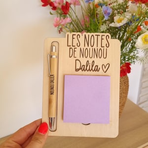 May include: A wooden memo board with a pen and a purple sticky note. The board has the text "LES NOTES DE NOUNOU Dalila" and a heart symbol. The pen is engraved with "NOUNOU DALILA".