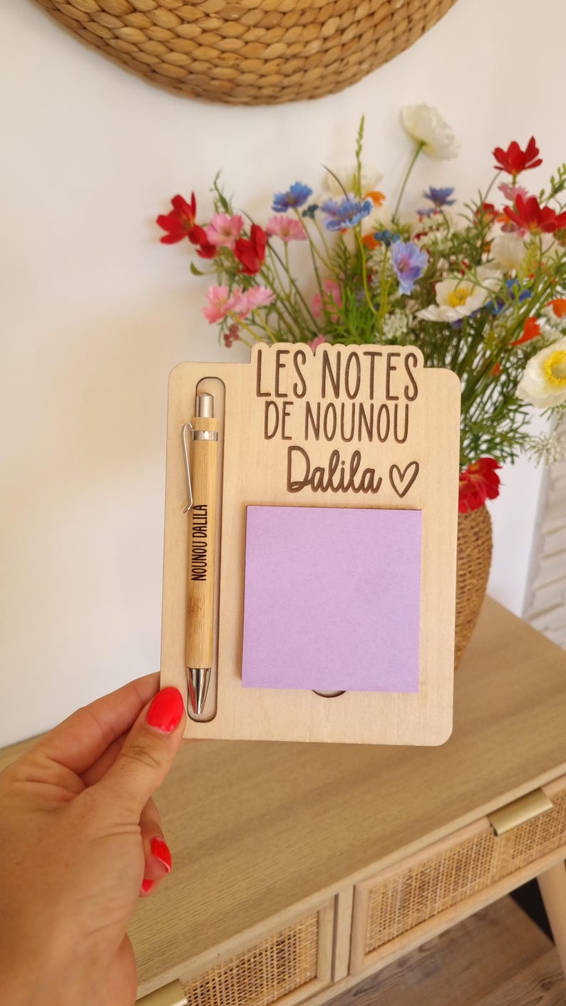May include: A wooden memo board with a pen and a purple sticky note. The board has the text "LES NOTES DE NOUNOU Dalila" and a heart symbol. The pen is engraved with "NOUNOU DALILA".