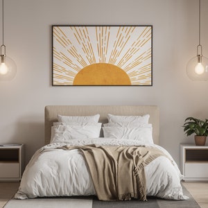 Puede incluir: Un dormitorio con una cama blanca, una manta marr&oacute;n y dos mesitas de noche. Las paredes son blancas y hay una impresi&oacute;n enmarcada de un sol amarillo con rayos blancos sobre la cama.