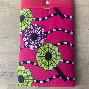 Peut inclure: Une pochette en tissu rose avec une fermeture à bouton blanc. La pochette présente un motif floral coloré avec des fleurs vertes, violettes et noires sur un fond rose.