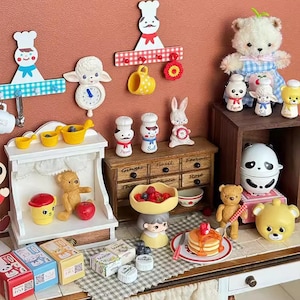 May include: A miniature kitchen playset with a variety of accessories, including a wooden countertop, a miniature oven, a set of miniature spice jars, a miniature teddy bear, a miniature panda, a miniature teapot, a miniature plate of pancakes, and a miniature bowl of fruit.