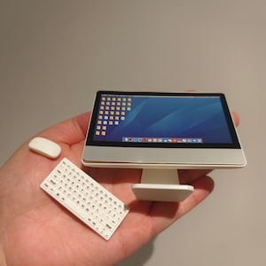 Può includere: Set di computer in miniatura con monitor argento e bianco, tastiera e mouse. Il monitor mostra uno sfondo blu del desktop. La tastiera ha tasti bianchi con lettere nere. Il set è una replica in scala ridotta.