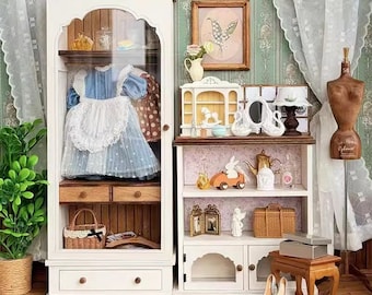 May include: A white wooden dollhouse with two cabinets, one with glass doors and shelves, and the other with a closed door and drawers. The cabinets are decorated with floral wallpaper and have a variety of miniature furniture and accessories inside, including a rocking horse, a tea set, and a doll.