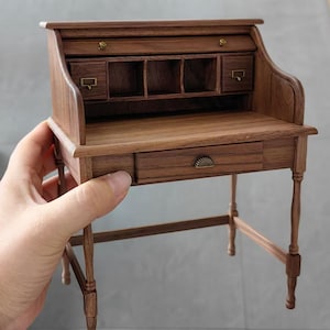 May include: A miniature wooden desk with a drop-down front, a drawer, and a shelf with compartments. The desk is made of dark wood with brass accents.