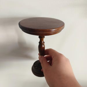 May include: A small, round, wooden table with a single, turned leg and a carved base. The table is dark brown and has a smooth, polished finish.