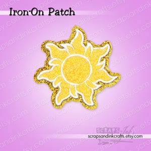 May include: An iron-on patch featuring a stylized yellow sun design with a central circular core and radiating pointed rays. The patch has a textured yellow surface, a white border, and a shimmering gold-colored edge against a light purple background.