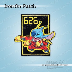 May include: An iron-on patch featuring the character Stitch from Lilo & Stitch. The patch is black with a yellow border and includes the number 626. Stitch is blue, red, and yellow, with a wide grin.
