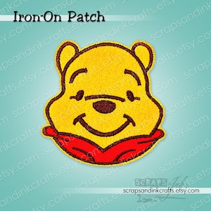 May include: Yellow embroidered iron-on patch featuring a smiling bear face with a red scarf. The patch has a black outline and the text "Iron-On Patch" at the top. The patch is a cheerful design for clothing or accessories.