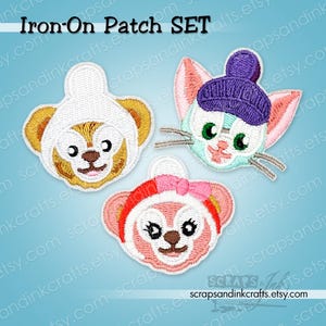 May include: An iron-on patch set featuring three embroidered character faces: a tan bear in a white hat, a light blue cat in a purple knit cap, and a pink bear with a red and pink headband. The text Iron-On Patch SET is visible at the top.